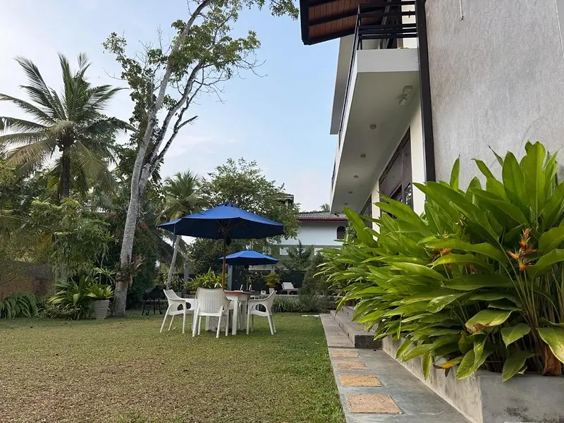 Outdoor dining tables under blue umbrellas on the lawn beside the house