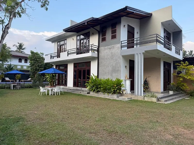 Two-storey villa with a wide lawn, garden furniture and blue parasols